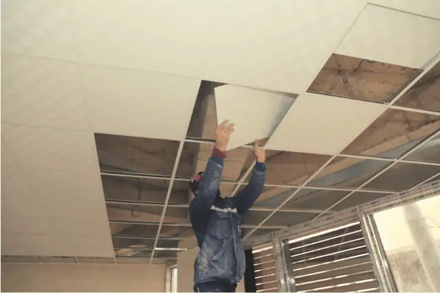 Man installing tiles on a suspended ceiling