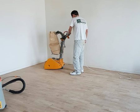Ludovic renovating the flooring by sanding the hardwood floor of his home